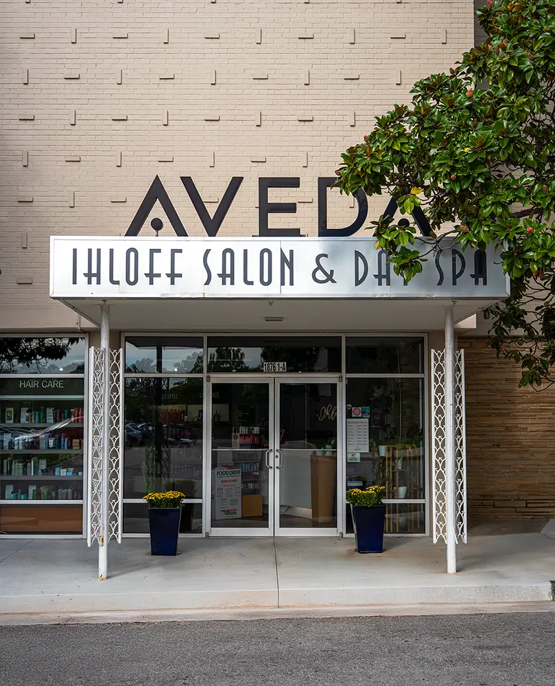The entrance of Ihloff Salon & Day Spa features large glass doors, a white awning, and two potted plants, inviting guests to experience exceptional salon services and rejuvenating spa treatments. - Ihloff Salon and Day Spa