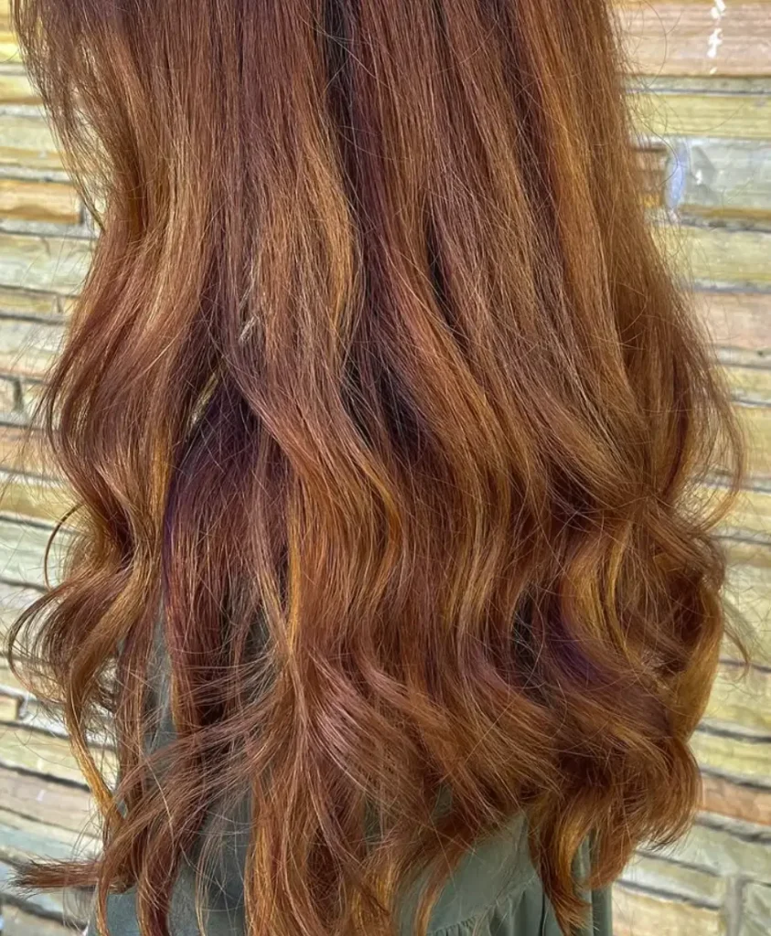 Long, wavy reddish-brown hair is shown from behind against a wooden plank background, highlighting a fresh hair style perfect for a spa day. - Ihloff Salon and Day Spa