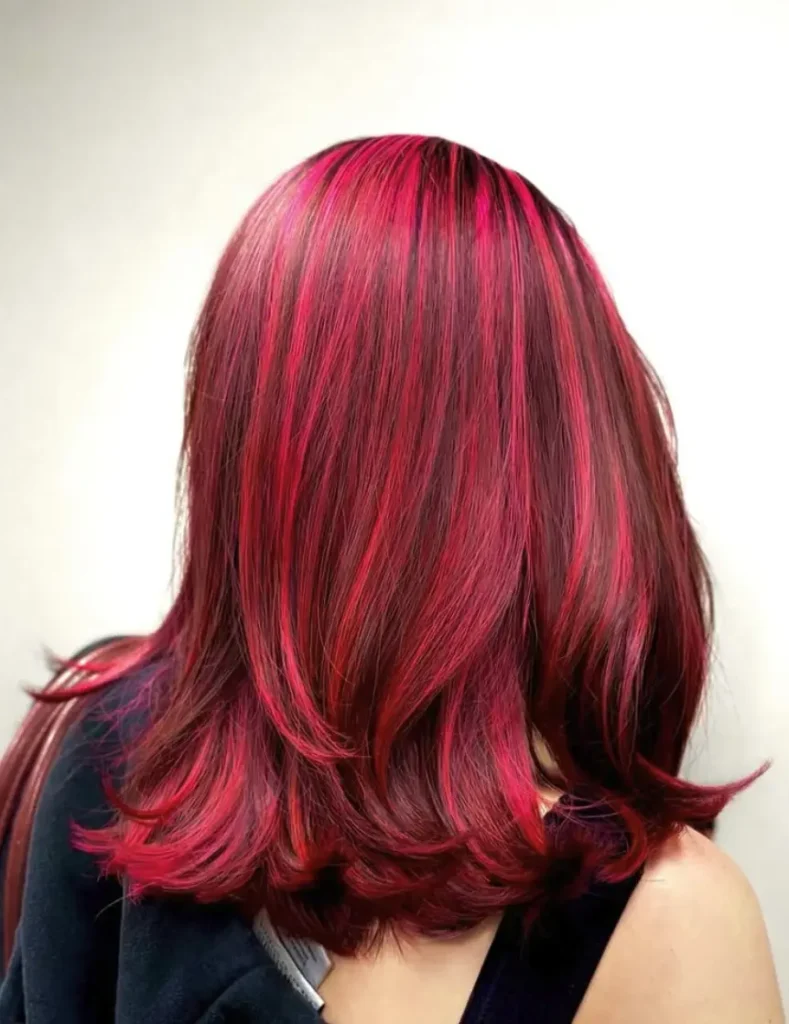 Person with shoulder-length, straight hair featuring vibrant red and magenta highlights, photographed from behind against a plain light background in a stylish salon setting. - Ihloff Salon and Day Spa